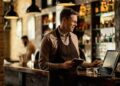 Happy barista adding an order to cash register while working in a pub.