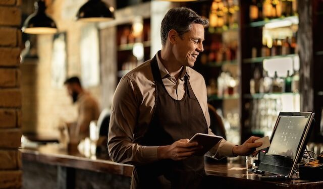 Happy barista adding an order to cash register while working in a pub.