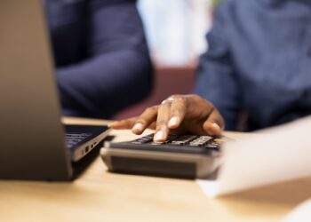 Man and woman reviewing bills and financial documents to track expenses, money management for a debt free lifestyle. Couple doing their household accounting with a calculator. Close up.