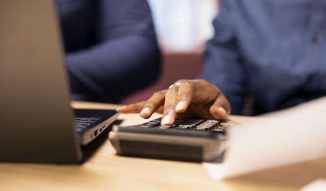 Man and woman reviewing bills and financial documents to track expenses, money management for a debt free lifestyle. Couple doing their household accounting with a calculator. Close up.